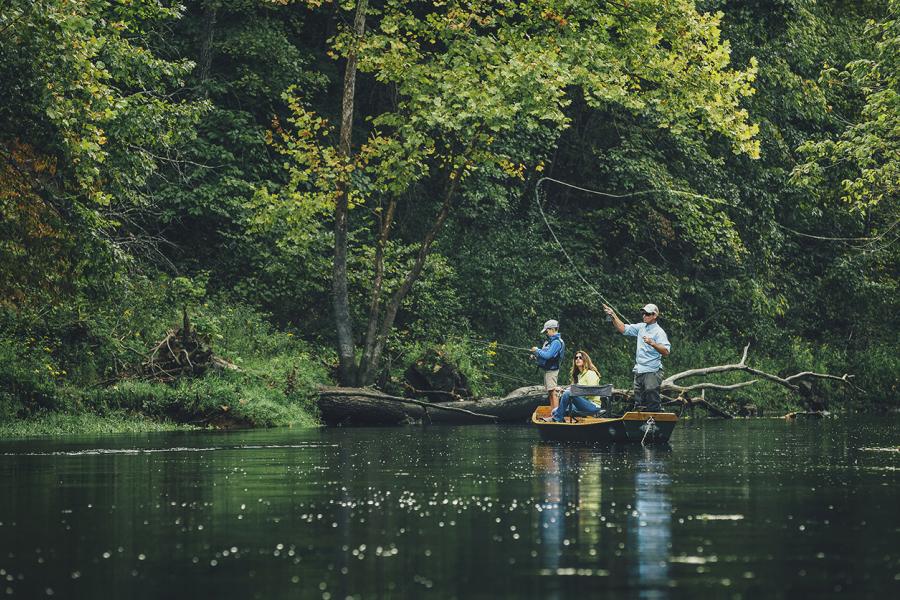 Father mother and son fly fish from a small boat in a lush wooded area on Lake Taneycomo