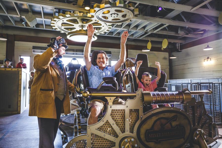 Father and son raising their arms in rollercoaster cart at the beginning of the ride.