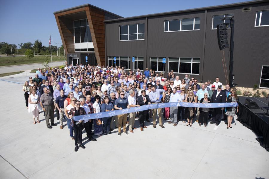 A large group of people cutting a giant ribbon in front of a building.