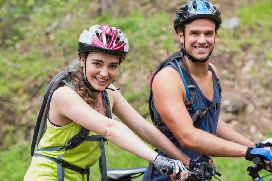 Man and woman wearing helmets and riding bicycles on a tree-lined trail in Branson. 