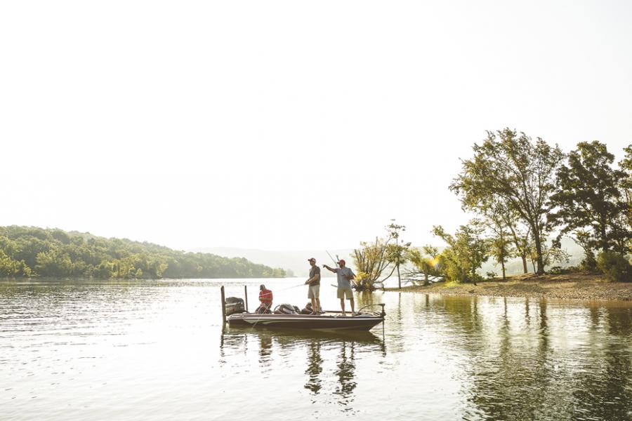 Three men fishing on fishing boat in the middle of scenic lake in Branson. 