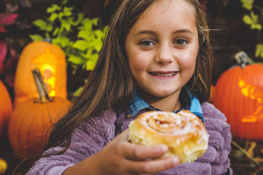 Young girl surrounded by pumpkins at a fall festival and eating a large cinnamon roll from a theme park in Branson.