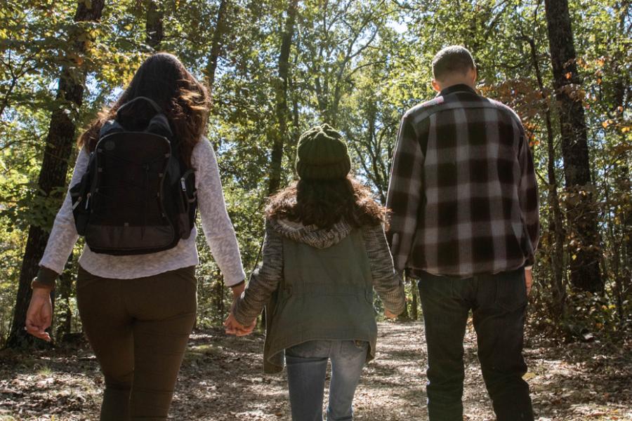 Father, mother and daughter holding hands and walking on wooded hiking trail in Branson.