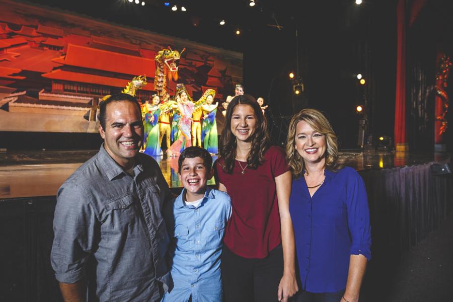 Family of four standing in front of a live show stage in Branson with Chinese acrobat performers on stage behind them.