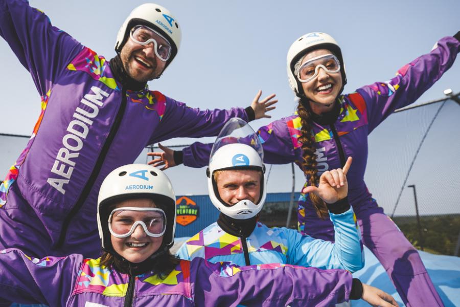 Family of three in purple suits about to fly with an instructor at an outdoor skydiving aerodium in Branson.