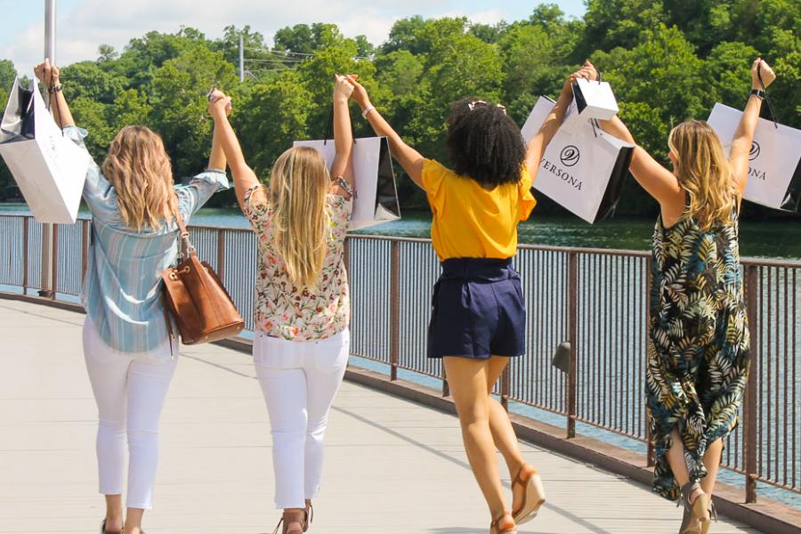 Four women holding hands and holding shopping bags at the Branson Landing for a girls' weekend getaway.