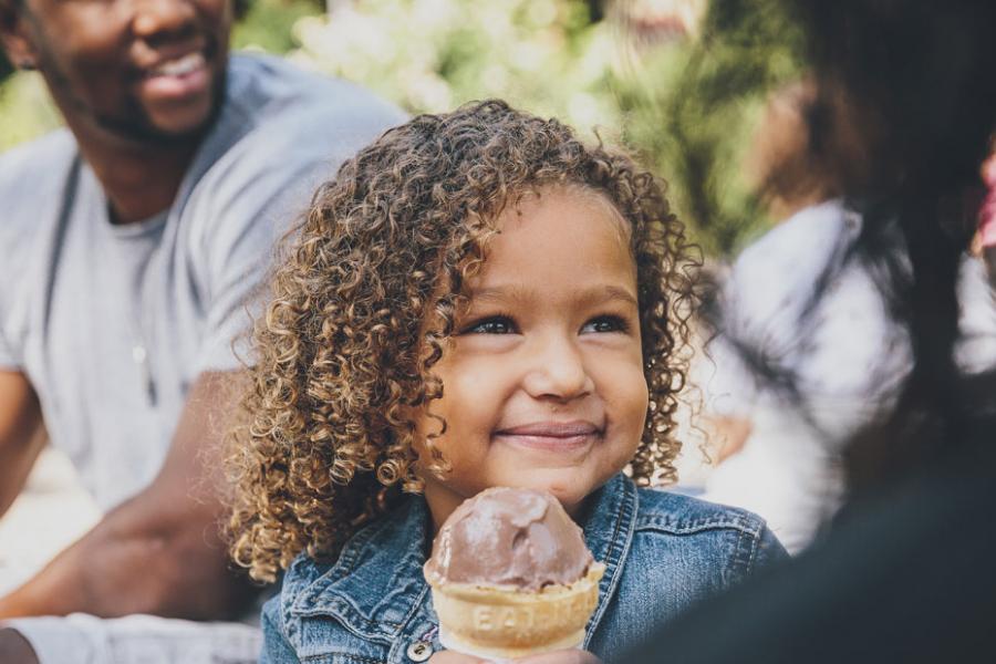 Young girl with black curly hair posing with a vanilla ice cream cone at a theme park in Branson.