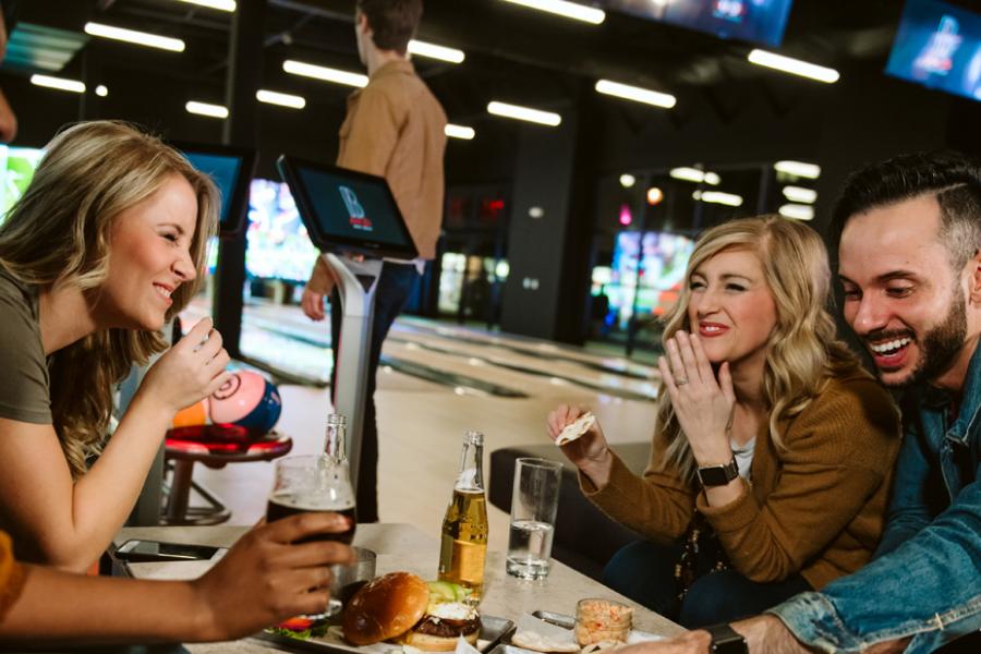 Group of friends eating and drinking at a bowling alley night club.