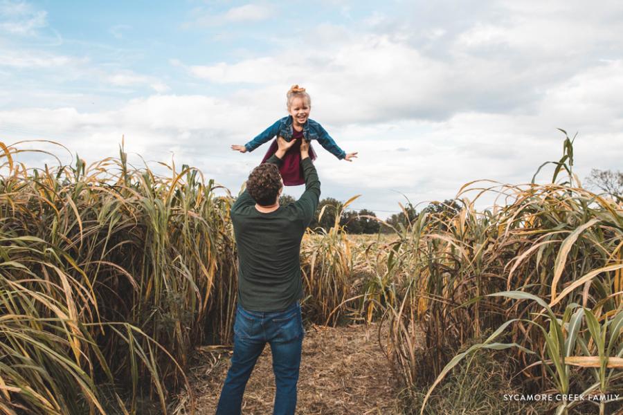 Dad holding daughter up in the air in the middle of a corn field.