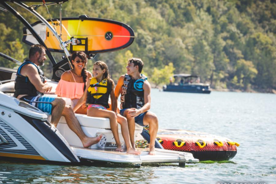 Family of four sitting on the back of a boat during summer, enjoying the Ozark Mountain scenery on a lake in Branson.