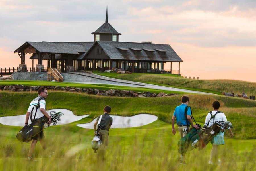 Group of four golfers walking toward clubhouse during sunset.