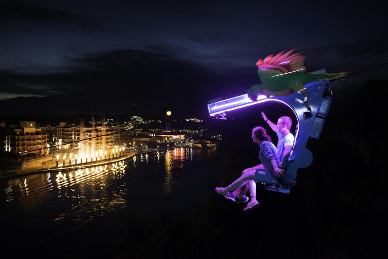 Two people ziplining across the lake at night.