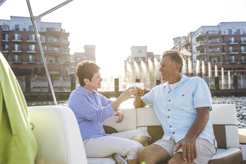 Man and woman sitting on boating on Lake Taneycomo with Branson Landing fountain in the background.