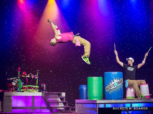 Two men drumming on buckets and boards on a live show stage in Branson.