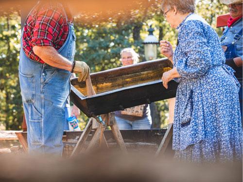 Two men and a woman wearing 1880s costumes making apple butter at a theme park in Branson.