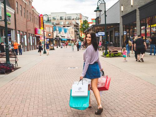 Young woman holding shopping bags and walking through outdoor shopping center in Branson.