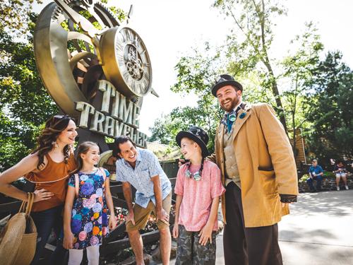 Family of four standing in front of Time Traveler roller coaster with Silver Dollar City staff member.